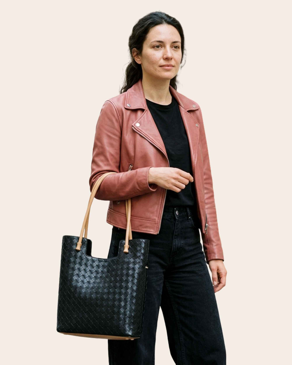 Woman in a pink leather jacket carrying the Nest woven leather tote in black