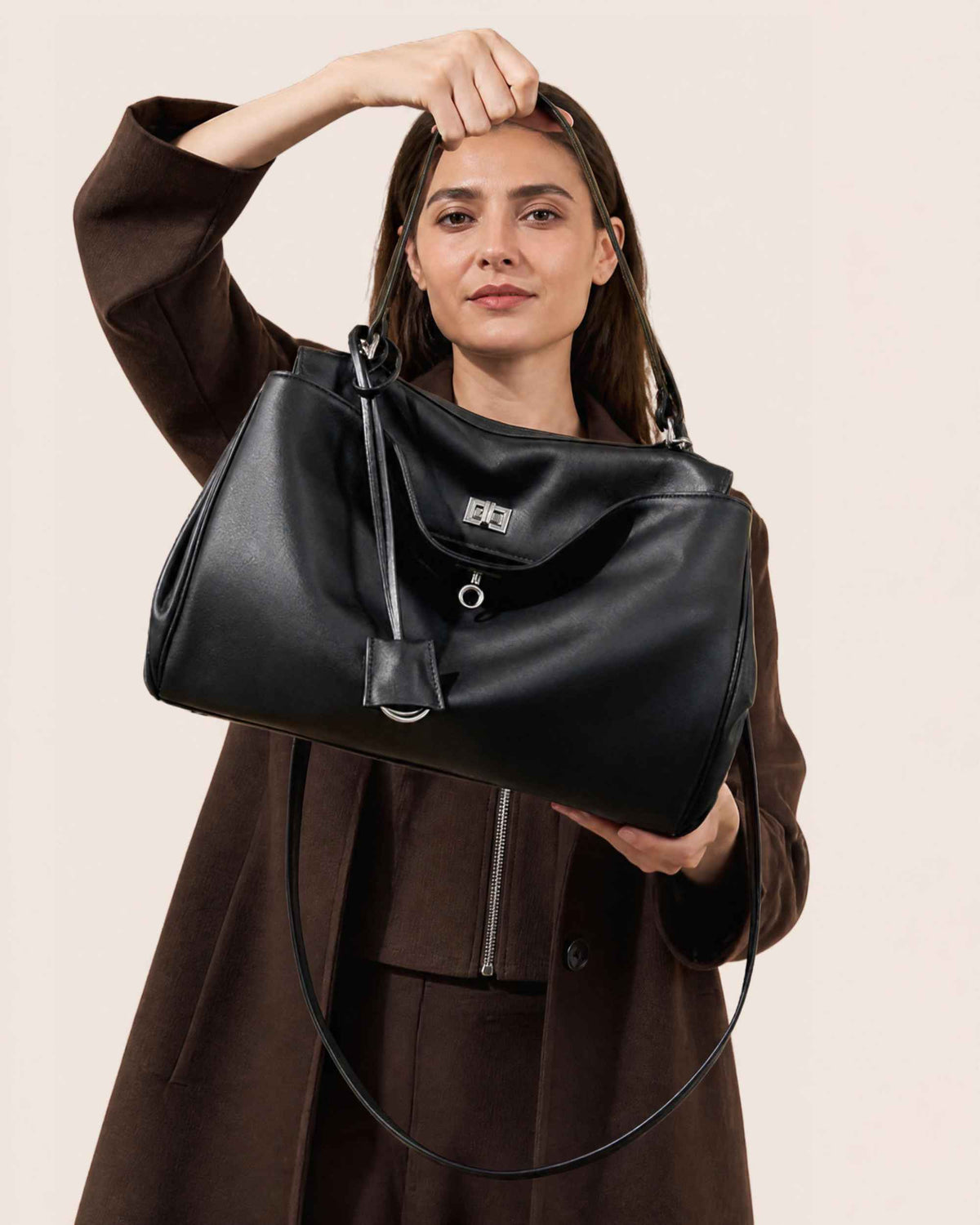 Woman in a brown coat holding the black leather flap bag by its long strap